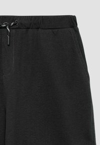 Zwarte trainingsbroek met een elastische tailleband, trekkoord en zijzakken. Gemaakt van zachte, gestructureerde stof met contrasterende stikseldetails.