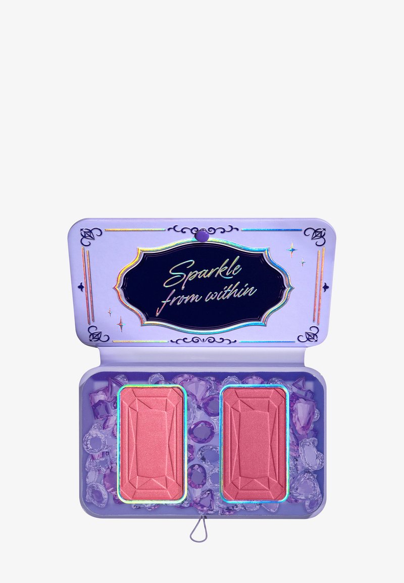 Compact avec une finition métallique violette contenant deux fards à joues en forme de diamant rose, entourés de faux bijoux. Le texte dit "Éclairez de l'intérieur."