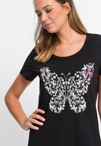 T-shirt nero con una grande grafica di farfalla bianca decorata con motivi floreali, accentuata da una piccola farfalla rosa, realizzata in tessuto morbido.
