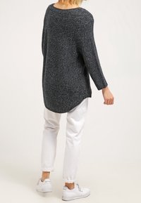 Mörkgrå stickad tröja med avslappnad passform, rundad halsringning och trekvartslånga ärmar, i kombination med vita byxor och vita sneakers.