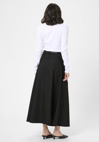 Falda larga negra con una silueta fluida, tela suave, detalles en la cintura, y combinada con mules negros de tacón y una blusa blanca ajustada.
