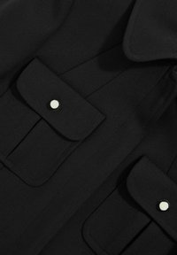 Schwarzes Stoffhemd mit zwei Brusttaschen mit Druckknopfverschluss, strukturiertem Kragen und strukturierter Oberfläche. Klare Linien und minimales Design.