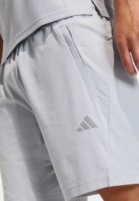 Light gray athletic shorts made from breathable fabric, featuring a subtle texture, side pockets, and a tonal logo accent.