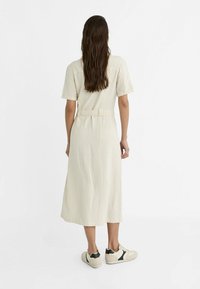 Beżowa lniana sukienka o luźnym kroju, z krótkimi rękawami, z paskiem w talii i midi długości, w połączeniu z kremowo-czarnymi sneakersami.