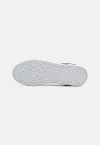 Semelle de chaussure en caoutchouc blanc texturé avec un motif en losange, contrastant avec une bande supérieure en cuir marron.