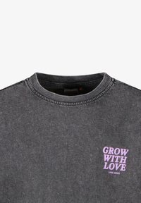 Donkergrijze katoenen t-shirt met ronde hals en korte mouwen. Kenmerkt de tekst "GROW WITH LOVE" in paarse letters op de linkerborst.