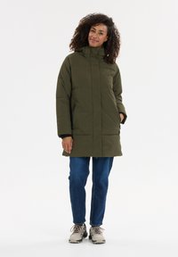 Oliven grøn isoleret pufferjakke med høj krave, lynlåslukning ved sidelommerne og en afslappet pasform, parret med blå jeans og grå sneakers.