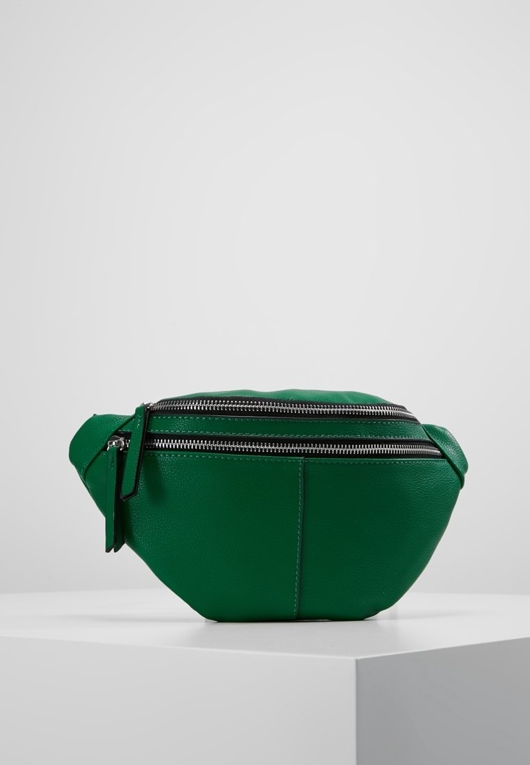 Sac banane en cuir vert avec deux fermetures éclair argentées et des tirettes noires, posé sur un piédestal blanc sur un fond gris uni.