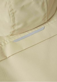 Tessuto impermeabile beige con una superficie liscia presenta una striscia riflettente argento e una cucitura ordinata lungo i bordi, indicando un design di qualità.