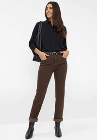 Pantalons en coton marron avec une coupe droite, ourlets retroussés, associés à une chemise noire et un sac à main noir. Les bottes présentent un design épuré.