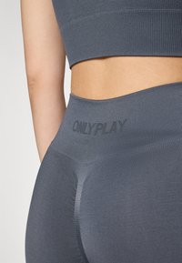 Sive sportske tajice s visokim pojasom, s rebrastom teksturom i suptilno prikazanim imenom brenda "ONLYPLAY" sprijeda.