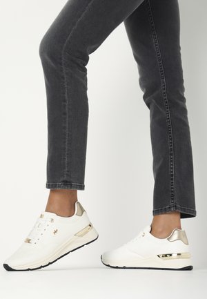 Weiße Sportschuhe mit goldenen Akzenten, strukturiertem Obermaterial und einem schlanken, flachen Design. Features eine schwarze Sohle und perforierte Details.