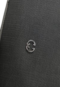 Materiale nero testurizzato con un'accattivante accentuazione argento del logo, design circolare con una sezione aperta, posizionato centralmente sulla superficie.
