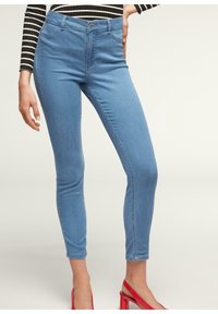 Vaqueros skinny de color azul claro con cintura alta, que cuentan con un cierre de botón y cremallera, bolsillos delanteros y una sutil textura elástica.