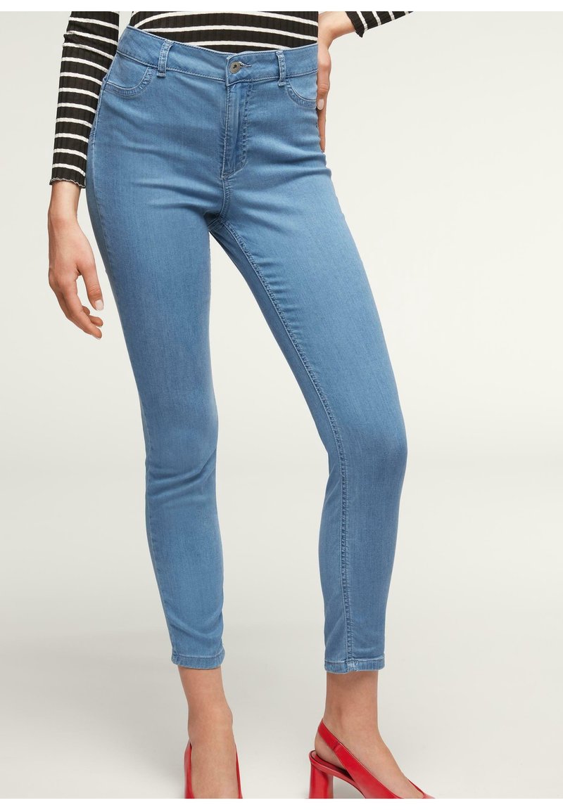 Vaqueros skinny de color azul claro con cintura alta, que cuentan con un cierre de botón y cremallera, bolsillos delanteros y una sutil textura elástica.