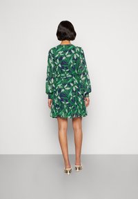 Vihreä ja laivastonsininen lyhythihainen mekko, jossa on lehtikuvio, röyhelöhelma ja vyötärönauha, valmistettu kevyestä kankaasta.