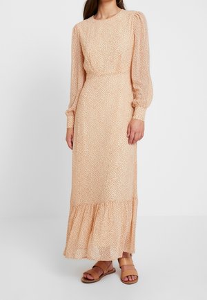 Woman wearing a long peach dress with small floral print, puffed long sleeves, and ruffled hem paired with tan flat sandals.