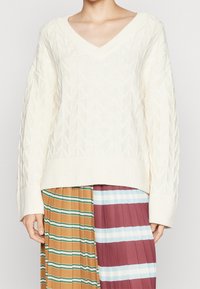 Pullover en tricot de couleur crème avec un motif géométrique texturé, un col en V large et des manches et un ourlet côtelés.