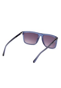Gafas de sol con tinte azul y montura cuadrada, lentes degradados y acabado brillante. Cuentan con varillas delgadas, protectoras contra los rayos UV, y acentos metálicos.