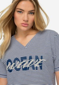 Koszulka V-neck w niebiesko-białe paski z odważnym wzorem graficznym zawierającym słowo "OCEAN" w ciemnoniebieskim i jasnoszarym kolorze.