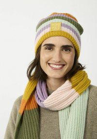 Gebreide gele, groene, paarse en roze gestreepte beanie met een embleem; bijpassende meerkleurige geribbelde sjaal met zachte texturen.