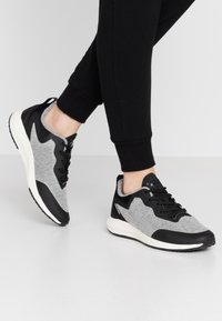 Baskets de sport grises et noires avec une tige texturée, un design épuré, une semelle blanche rembourrée et des lacets noirs.