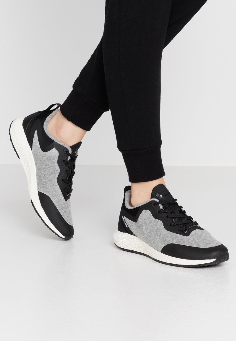Baskets de sport grises et noires avec une tige texturée, un design épuré, une semelle blanche rembourrée et des lacets noirs.