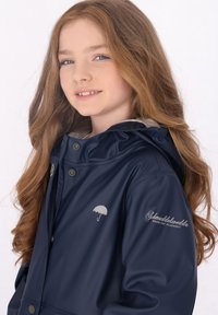 Jūros mėlynumo vandeniui atsparus švarkas su kapišonu, sidabriniu skėčio logotipu ant krūtinės ir sidabriniu tekstu ant rankovės. Lygus paviršius su snapų užsegimais.