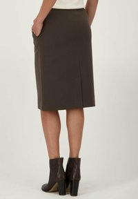 Jupe marron de longueur genou avec une coupe droite, poches latérales et une fente au dos, associée à des bottines châtaigne à talon épais.