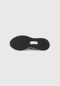 Semelle de chaussure de sport avec une surface en caoutchouc noir texturé, présentant un motif de semelle et une découpe centrale pour plus de flexibilité.