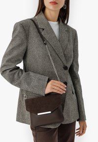 Borsa a tracolla in pelle marrone e suede con chiusura a pattina, hardware in argento e tracolla a catena. Texture morbida, design minimalista.