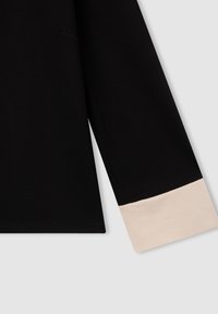 Maglietta nera a maniche lunghe con dettagli beige sui polsini contro uno sfondo grigio chiaro.