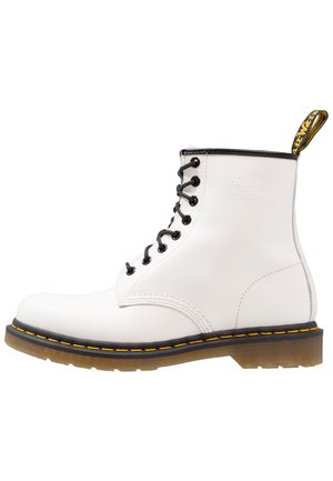 Stivaletto bianco in pelle con lacci neri, cuciture gialle e un cinturino per il tallone. Texture liscia con una forma della punta arrotondata.