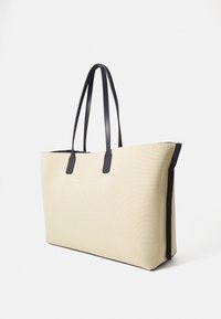 Bolso tote de lienzo beige con asas de cuero negro; forma rectangular y superficie texturizada; cuenta con ribete negro a lo largo de los bordes.