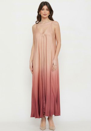 Donna in piedi che indossa un abito maxi senza maniche scollo a V sfumato nei toni dal beige al rosa intenso, abbinato a décolleté beige con punta.