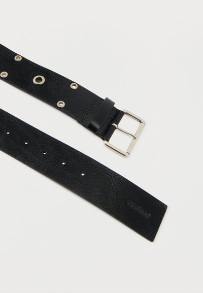 Ceinture en cuir noir avec boucle en argent et plusieurs œillets métalliques sur fond blanc, montrant les côtés avant et arrière.