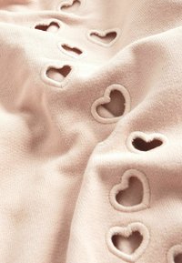 Tessuto rosa chiaro con dei ritagli a forma di cuore, bordato da un morbido profilo strutturato. Il materiale sembra elastico e leggermente testurizzato.