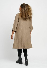 Lång, lös klänning i en strukturerad taupe-färg med trekvartsärmar, kombinera med svarta leggings och anklarboots.