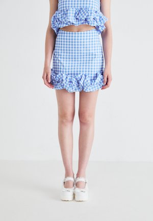 Blå og hvit rutete crop top og miniskjørt sett med volanger. Hvite platå sko med dekorative stropper og sløyfer.