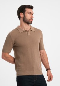 Kortærmet polo-shirt i beige strikstof. Har en klassisk krave, to knapper og ribbede manchetter. Glat tekstur, tætsiddende design.