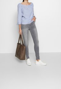 Blusa de tirantes azul y blanca a rayas, pantalones ajustados grises, zapatillas blancas y un bolso tote marrón con dos asas.