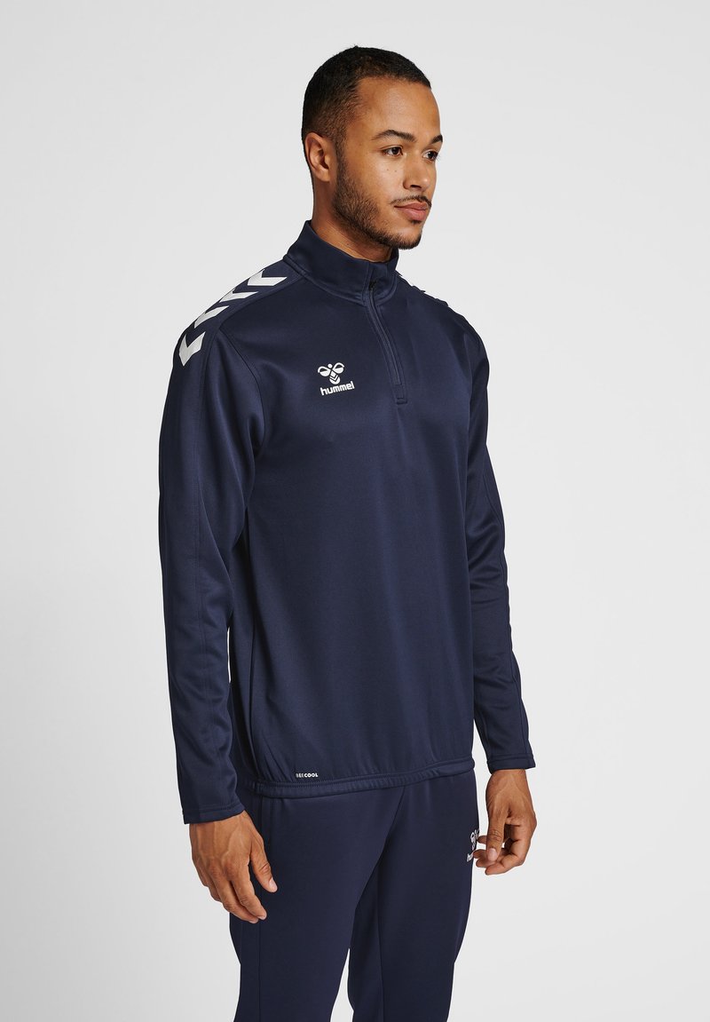 Marine blauwe sportieve zip-up jack met lange mouwen, met een hoge kraag en wit logo. Inclusief contrasterend schouder chevron ontwerp.