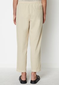 Beige leichte Hose mit elastischem Bund, mit einer Gesäßtasche und leicht taillierten Beinen, die in umgeschlagenen Säumen enden.