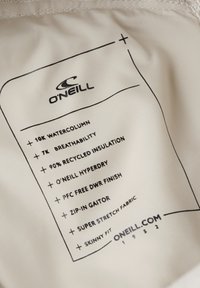 O'Neill zīmols attēlots uz viegla auduma. Teksts norāda īpašības: 10K ūdens statums, 7K gaisa caurlaidība, 90% atkārtoti pārstrādātas izolācijas un citas.