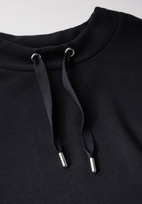 Svart sweatshirtkrage med ribbad textur, som har silverfärgade öglor och matchande svarta dragsnören. Närbild som framhäver materialdetaljer.