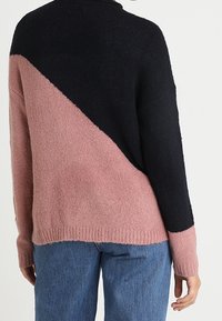 Stickad tröja med diagonal design; svart övre halva och rosa nedre halva. Mjuk textur, ribbad nederkant och mudd vid ärmslut.