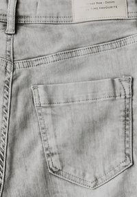 Tela de mezclilla gris claro con un diseño clásico de cinco bolsillos. Presenta un bolsillo trasero cosido y una etiqueta de marca en la cintura.