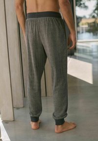 Graue Jogginghosen mit Fischgrätenmuster, einem schwarzen elastischen Bund und gerippten Bündchen, die einen lockeren Schnitt aufweisen.