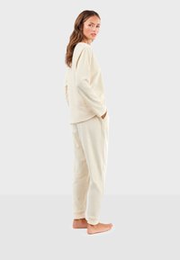 Ensemble de vêtements de détente de couleur crème, fabriqué en tissu doux, comprenant un haut à manches longues et un pantalon fuselé avec poches. Motif à pois subtil sur l'ensemble.