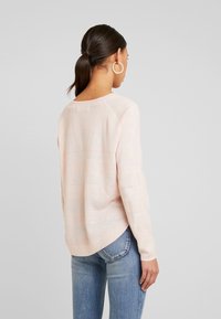 Hellrosa gestrickter Pullover mit strukturierten Streifen, weitem Ausschnitt und gerippten Bündchen, kombiniert mit blauer Jeans, von hinten betrachtet.